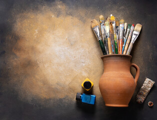 Poster - Paint brush in clay jug and art painter tool on abstract background texture. Paintbrush painting