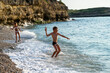 © sommersby - Two kids playing on gravel beach at sea in bright sunshine. Caucasian boy stands on beach in summer and throws pebbles into sea.
