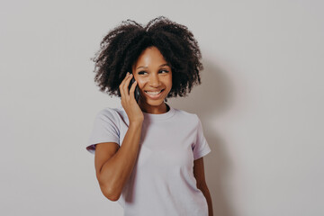 Wall Mural - Studio portrait of cheerful dark skinned woman enjoying conversation on mobile phone