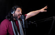 © Nailotl - View of a Hispanic man with beard wearing a scarf and a headset recording podcast in the studio