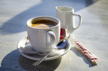 Sticker - Closeup shot of a cup of coffee with plate, silver spoon and a milk jug isolated on a table