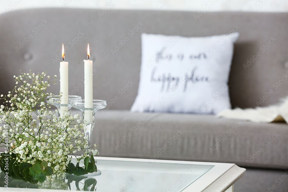 Burning candles with flowers and plant branches on table in room - obrazy, fototapety, plakaty 