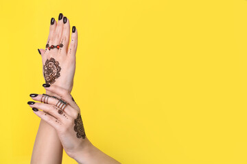 Wall Mural - Woman with henna tattoos on hands against yellow background, closeup and space for text. Traditional mehndi ornament