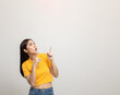 © Chanakon - Excited asian woman pointing the finger to blank space over head for advertising text on isolated background. Joyful teenage girl in yellow shirt standing in white room looking at empty space.