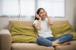 © Chanakon - Relaxing time on sofa. Beautiful young asian woman sitting on sofa she choose music from smartphone take a rest and listening song with headphone. Lifestyle in living room at house in the morning.
