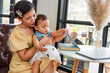 © Subhakitnibhat - A happy Chinese Asian mother and her young daughter are interested in morning books together in the living room at home. family activity concept.