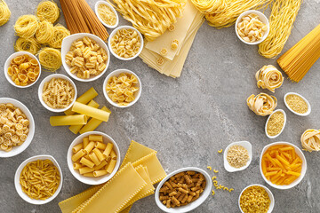 Poster - Pasta. Various kinds of uncooked pasta and noodles over stone background, top view with copy space for text. Italian food culinary concept. Collection of different raw pasta on cooking table