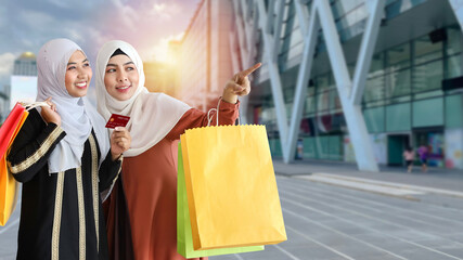 Asian lifestyle tourist traveller concept. Young shopper muslim women with shopping bags and holding credit, pointing finger something to destination city building with shopping mall background