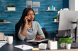 © DC Studio - Black student sitting at desk table in living room working at high school homework discussing with collegue using smartphone. African woman searching online webinar ideas using elearning platform