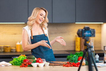 Young woman prepares food and hosts a cooking show. The blogger streams from modern kitchen. Vegetarian healthy food preparation.