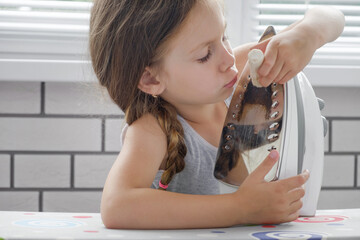 The girl child cleans the sole of the iron with a special cleaning pencil, cleaning the iron from carbon deposits, close-up