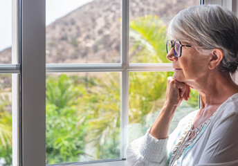 Pensive elderly woman at the window looking out