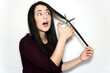 © AliciaFdez - Beautiful brunette woman with a surprised face cutting her long hair with scissors on a white background. Shocked girl