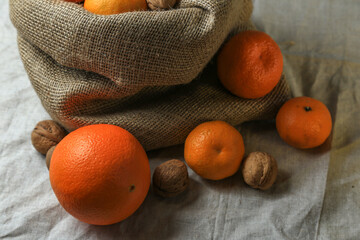 Ripe, tasty and juicy oranges, tangerines in a canvas bag with walnuts on the table.