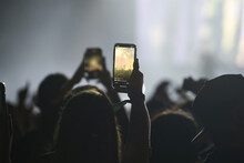 Silhouette of a unrecognizable woman holding an smartphone in a concert
