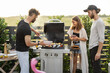 Young friends cooking vegetables and fish on a modern gas grill at backyard on a sunset. Eating and spending summer time outdoors