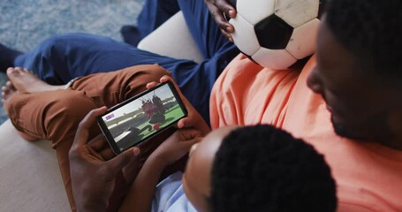 Wall Mural - Composite of father and son at home watching hockey match on smartphone