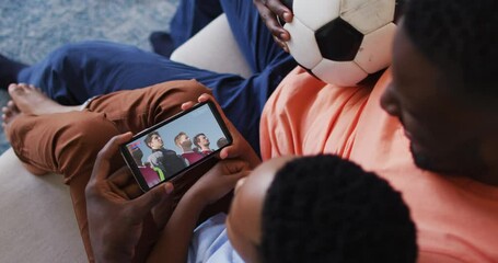 Wall Mural - Composite of father and son at home watching sports event on smartphone