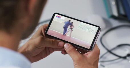 Wall Mural - Composite of male doctor watching judo match on smartphone