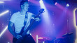 © Gorodenkoff - Rock Band Performing at a Concert in a Night Club. Portrait of a Lead Guitarist Playing on a Guitar. Live Music Party in Front of Bright Colorful Strobing Lights on Stage.