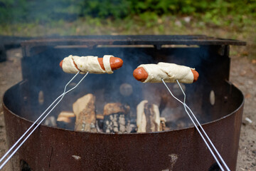 Hot dogs wrapped in the dough are being roasted over the campfire