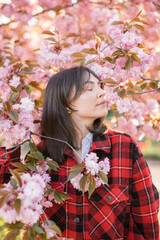 Outdoor portrait of young beautiful Caucasian teen girl smiling and looking into camera, blossom par full of cherry trees on a windy day. 4K footage with sunlight rays