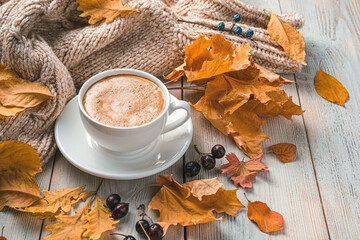 A cup of coffee on an autumn morning against the background of foliage and a sweater.