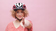 © CameraCraft - Beautiful young girl wearing a bicycle helmet smiling and pointing at the camera. The girl is dressed in a casual pink top. Cycling for leisure healthy lifestyle concept. Isolated over pink background