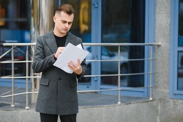 Serious business man reading documents at street. Confident businessman examining papers outdoor. Thoughtful man walking with documents at city street.