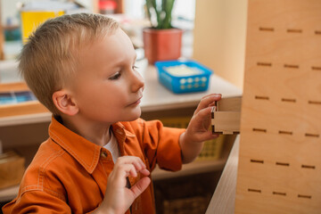 Wall Mural - kid opening cabinet in wooden box while playing cognitive game in montessori school