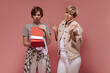 © Look! - Sad girl with short hairstyle in modern clothes holding opened gift box and posing with blonde old woman in white outfit on pink background..