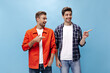 © Look! - Charming cheerful bearded men point at place for text on blue background. Portrait of guy in orange jacket and his friend in checkered shirt.
