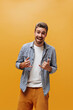 © Look! - Happy cheerful bearded man in stylish bright pants, blue checkered shirt rejoices, shows Shaka signs on orange background.