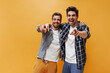 © Look! - Good-humored bearded young men in colorful pants, white t-shirts and plaid shirts point at camera, smiles on orange background.
