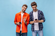 © Look! - Cheerful charming bearded men in stylish orange jacket and checkered shirt smile and hold phone on isolated blue background.