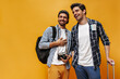 © Look! - Happy young cool brunet men in white t-shirts and checkered shirts rejoice, smile and pose on orange background. Travelers hold backpack and retro camera.