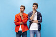 © Look! - Thoughtful young men in white t-shirts and stylish shirts look up. Guy in orange jacket and man in checkered shirt pose on blue background.