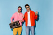© Look! - Cheerful happy friends have fun on blue isolated background. Brunet man in orange jacket and jeans holds beer bottle. Guy in yellow shorts and pink hoodie poses with record player.
