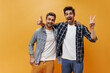 © Look! - Happy brunet bearded men in white t-shirts and plaid colorful shirts rejoice, smile and show thumbs up on orange background.