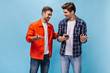 © Look! - Cheerful men talk on blue background and smile. Guy in checkered shirt holds phone. Friends pose on isolated backdrop.