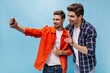 © Look! - Happy cheerful young men in orange jacket and checkered stylish shirt smile and take selfie on blue isolated background.