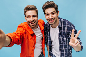 Wall Mural - Happy excited bearded men take selfie on blue background. Guy in orange jacket and man in checkered shirt smile on isolated.