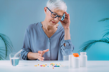 Wall Mural - Confused senior woman looking at her medicines on the table. Medicine non-adherence concept.