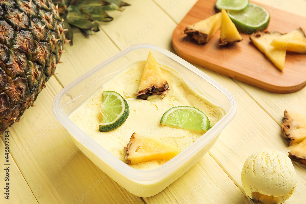 Container with tasty pineapple ice cream on color wooden background