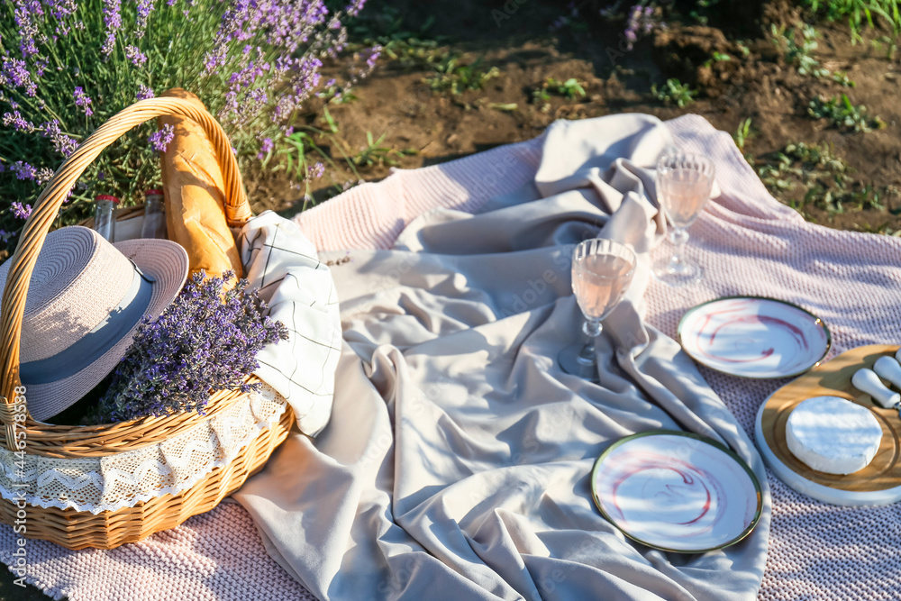 Wicker basket with drink and dinnerware for romantic picnic in lavender field - obrazy, fototapety, plakaty 
