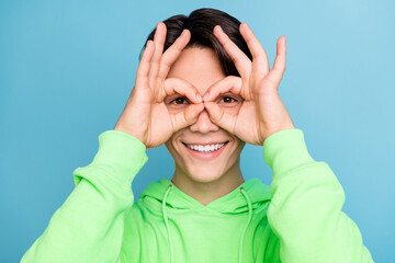 Sticker - Photo of funny foolish guy show okey sign cover eyes look camera wear green hoodie isolated blue color background