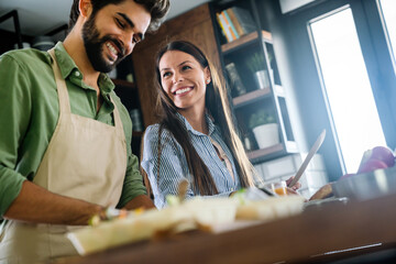 Wall Mural - Beautiful young couple is using a digital tablet and smiling while cooking in kitchen at home