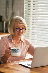 Smiling senior using laptop in the kitchen