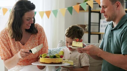 Wall Mural - family, holidays and people concept - portrait of happy mother, father and little son sharing birthday cake sitting on sofa at home party