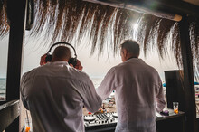 Back View Of Disc Jockeys Playing Music For Tourist People At Club Party Outdoors On The Beach - Djs Wearing Headphones At Music Live Event - Music And Fun Concept - Entertainment And Party Concept